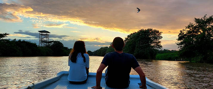 Deux personnes à l'avant d'un bateau en train d'admirer une fin de coucher de soleil sur une rivière